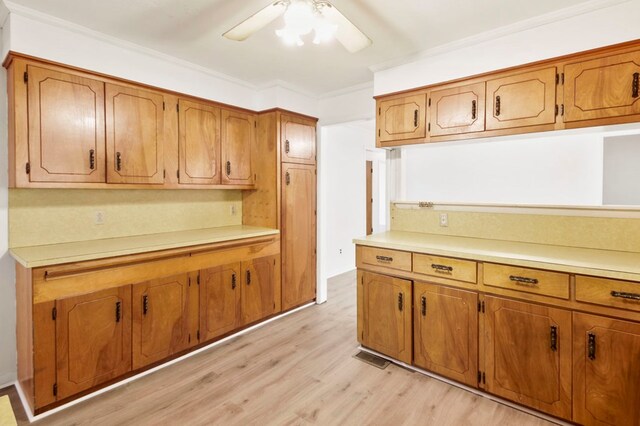 kitchen with a ceiling fan, light wood-style flooring, ornamental molding, brown cabinets, and light countertops