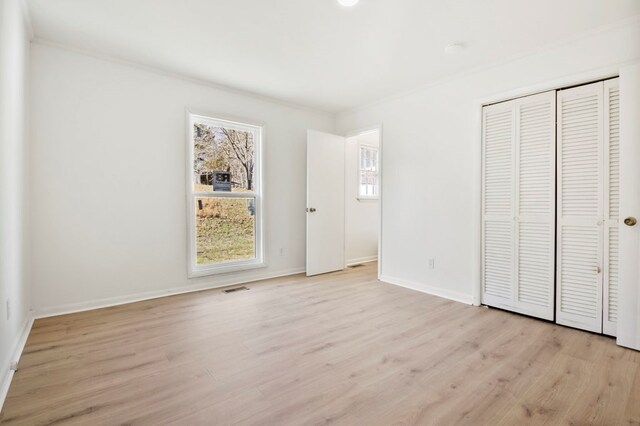 unfurnished bedroom featuring crown molding, a closet, visible vents, light wood-style flooring, and baseboards