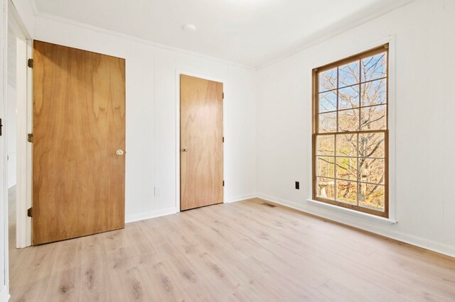 unfurnished bedroom featuring light wood-style floors, baseboards, visible vents, and crown molding