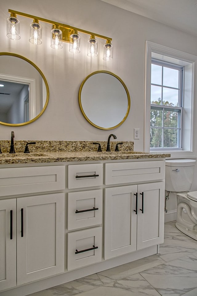 bathroom with double vanity, marble finish floor, toilet, and a sink