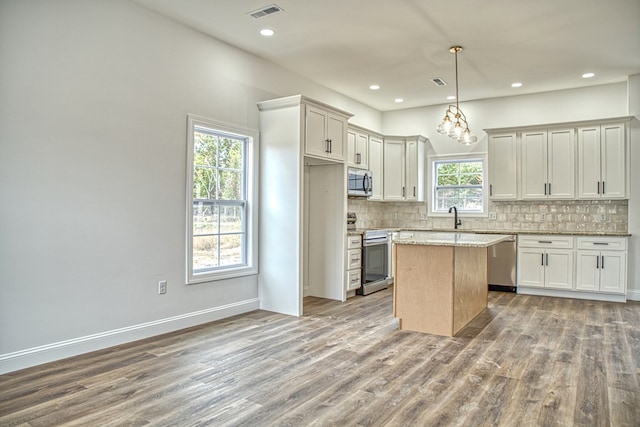 kitchen featuring decorative light fixtures, visible vents, appliances with stainless steel finishes, a kitchen island, and light stone countertops