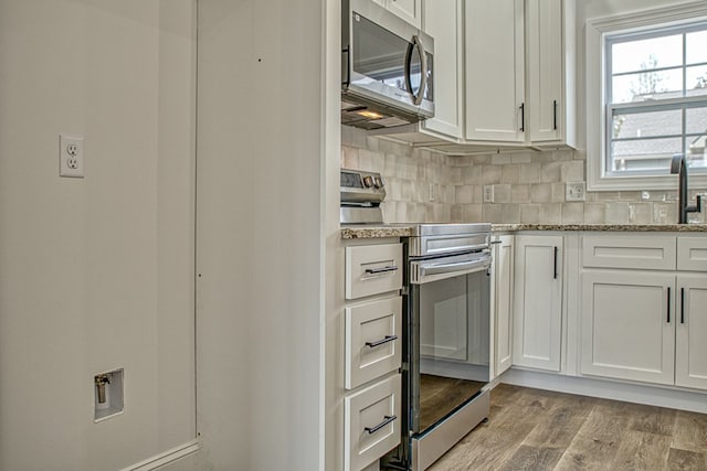 kitchen with appliances with stainless steel finishes, white cabinets, light wood finished floors, and tasteful backsplash