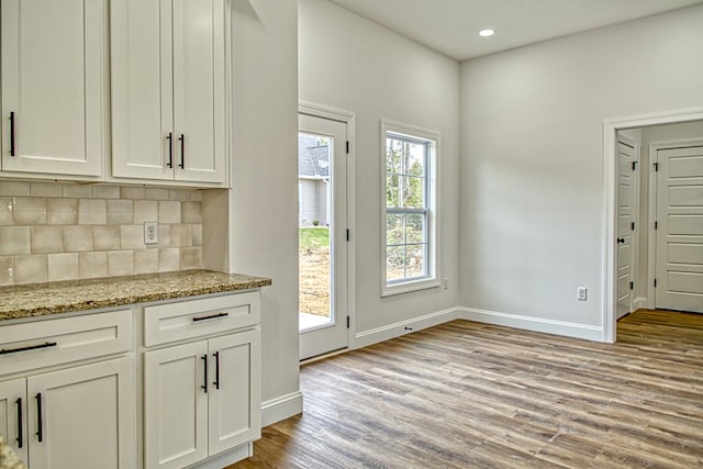 interior space with tasteful backsplash, light wood-style floors, white cabinetry, and light stone countertops