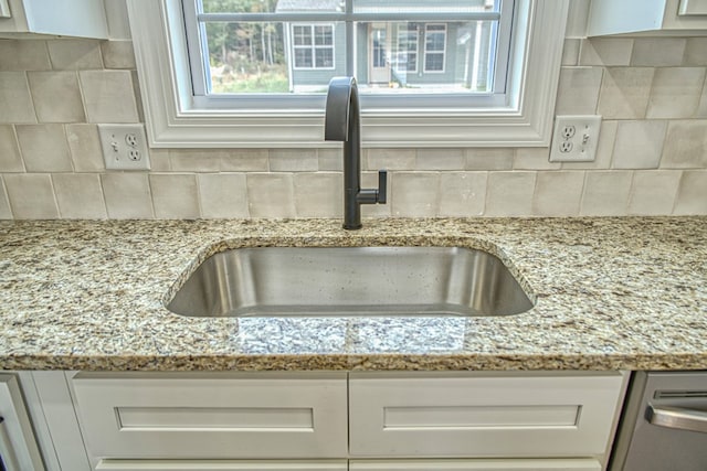 details with light stone counters, stainless steel dishwasher, decorative backsplash, white cabinets, and a sink