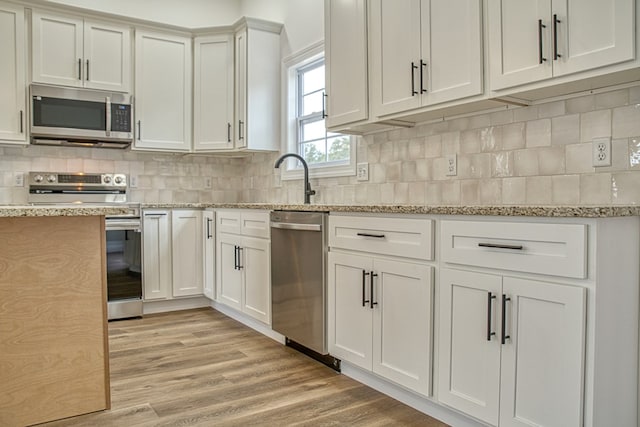 kitchen with light wood finished floors, tasteful backsplash, white cabinetry, and stainless steel appliances