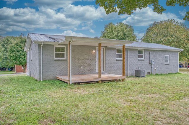 back of property featuring brick siding, metal roof, central AC, and a yard