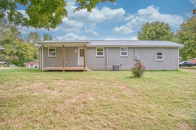 rear view of house featuring central AC, metal roof, a lawn, and brick siding