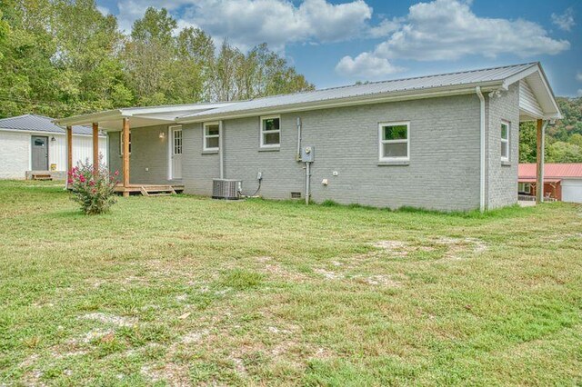 rear view of property with metal roof, a yard, brick siding, and central AC