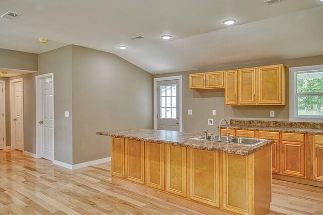 kitchen with baseboards, visible vents, a kitchen island with sink, light wood-type flooring, and a sink