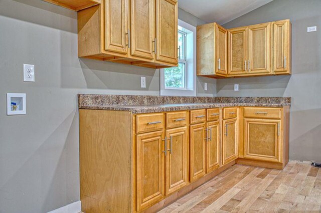 kitchen featuring light wood-style floors, dark countertops, and vaulted ceiling