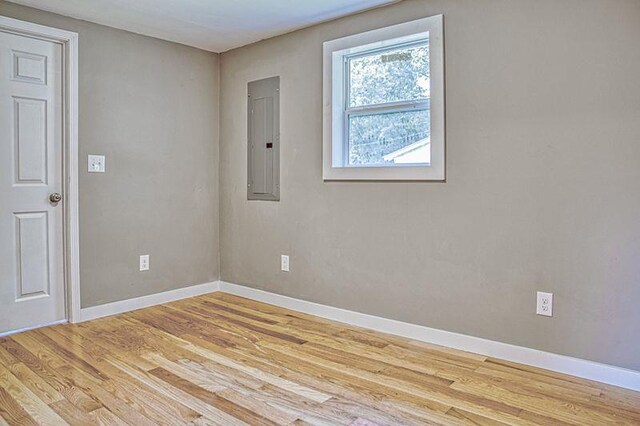 empty room with baseboards, electric panel, and light wood finished floors