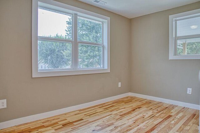 empty room with a healthy amount of sunlight, light wood-type flooring, visible vents, and baseboards