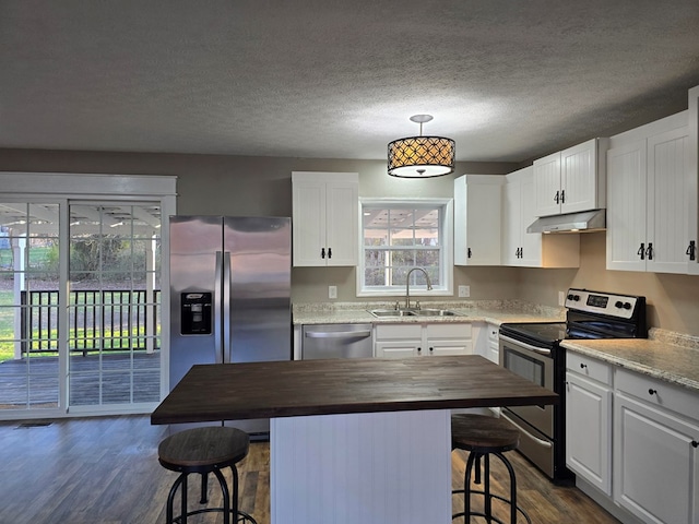 kitchen with a breakfast bar area, appliances with stainless steel finishes, under cabinet range hood, white cabinetry, and a sink