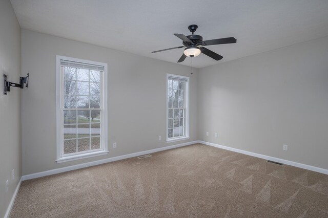 carpeted spare room featuring a healthy amount of sunlight, baseboards, and visible vents