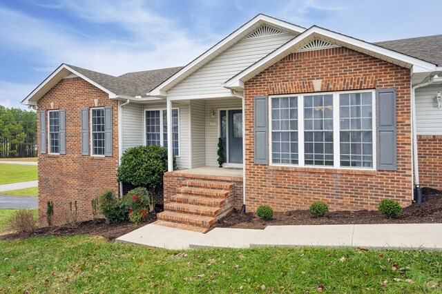 ranch-style house featuring a shingled roof, brick siding, and a front lawn