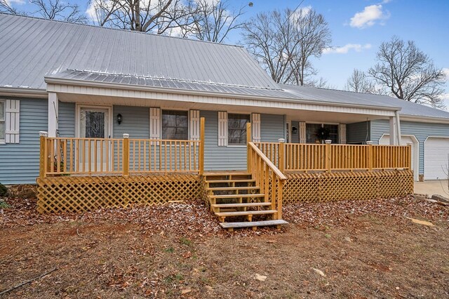 rear view of property with a garage, metal roof, stairs, and a porch