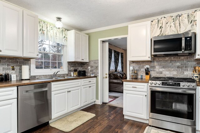 kitchen with appliances with stainless steel finishes, white cabinets, wooden counters, and a sink