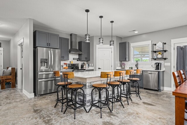 kitchen featuring a center island, wall chimney exhaust hood, stainless steel appliances, decorative backsplash, and a kitchen breakfast bar