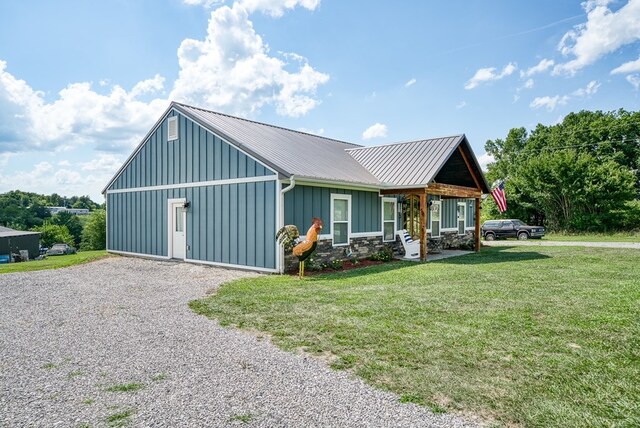 view of front of house with stone siding, metal roof, gravel driveway, board and batten siding, and a front yard