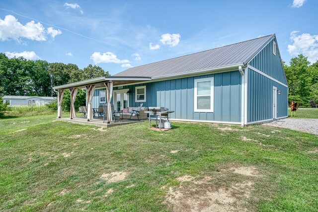 back of house featuring board and batten siding, metal roof, a lawn, and a patio