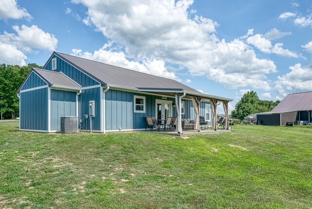 rear view of property featuring metal roof, a patio, cooling unit, a lawn, and board and batten siding