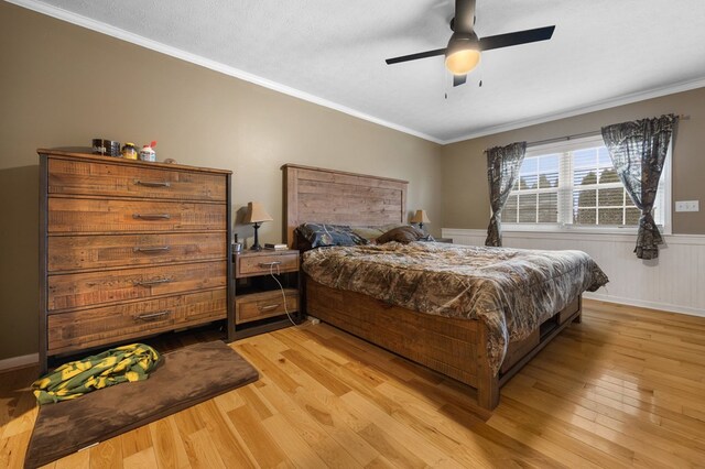 bedroom featuring a ceiling fan, wainscoting, ornamental molding, a textured ceiling, and light wood-type flooring