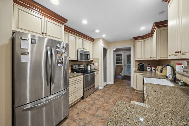 kitchen featuring stone countertops, appliances with stainless steel finishes, backsplash, cream cabinetry, and a sink