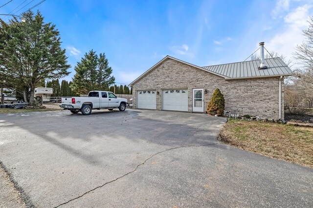 view of property exterior with aphalt driveway, brick siding, metal roof, and an attached garage