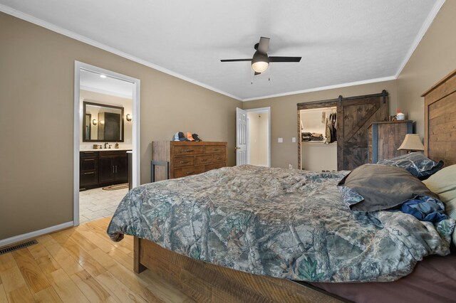 bedroom with ornamental molding, a barn door, light wood finished floors, and visible vents