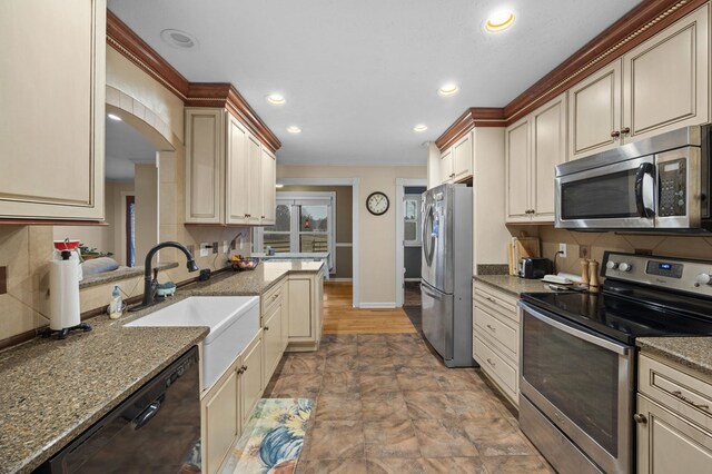 kitchen featuring stainless steel appliances, cream cabinetry, a sink, and backsplash