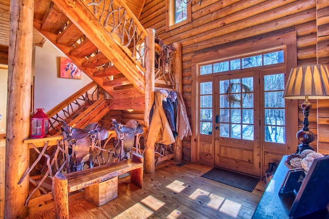 entrance foyer with stairs, rustic walls, wood-type flooring, and a towering ceiling