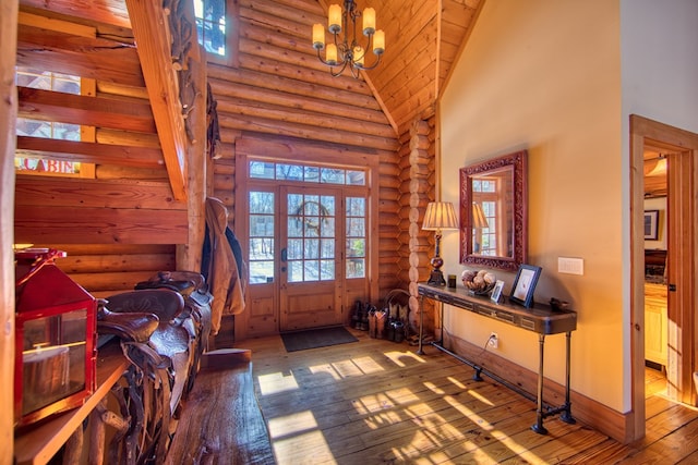 foyer entrance with log walls, an inviting chandelier, high vaulted ceiling, baseboards, and hardwood / wood-style flooring