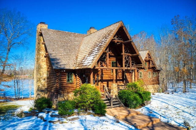 cabin featuring a porch, a chimney, and log siding