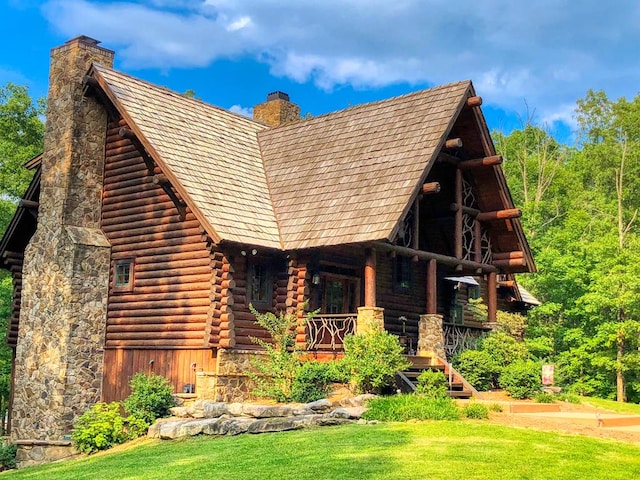 view of side of home featuring covered porch, log exterior, a chimney, and a lawn