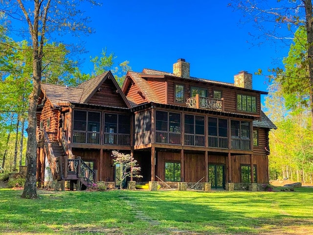 back of property featuring a sunroom, a chimney, stairway, and a lawn