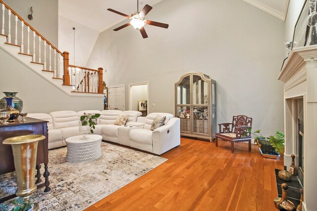 living area featuring ceiling fan, wood finished floors, a high ceiling, stairs, and crown molding