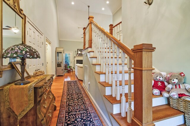 staircase featuring a towering ceiling, ornamental molding, wood finished floors, and recessed lighting