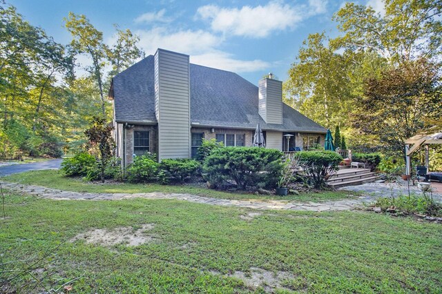 exterior space featuring roof with shingles, brick siding, a lawn, and a chimney