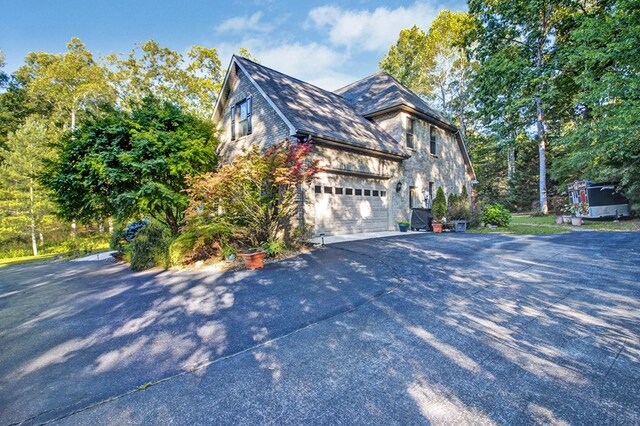 view of property exterior featuring a garage, stone siding, and driveway