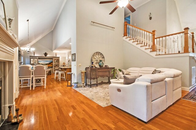 living area with stairs, a fireplace, wood finished floors, high vaulted ceiling, and ceiling fan with notable chandelier