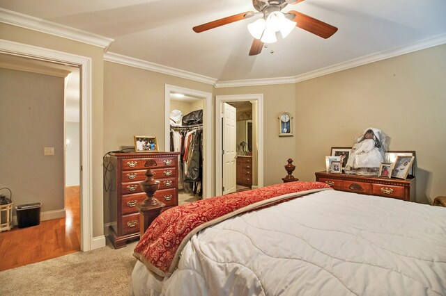 bedroom with light colored carpet, ceiling fan, a walk in closet, crown molding, and a closet