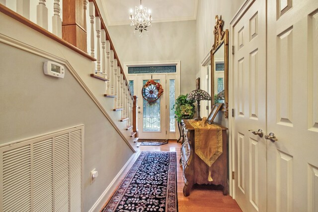 doorway to outside featuring a notable chandelier, wood finished floors, baseboards, stairs, and ornamental molding