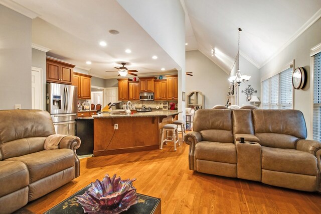 living area featuring ornamental molding, lofted ceiling, light wood finished floors, and ceiling fan with notable chandelier