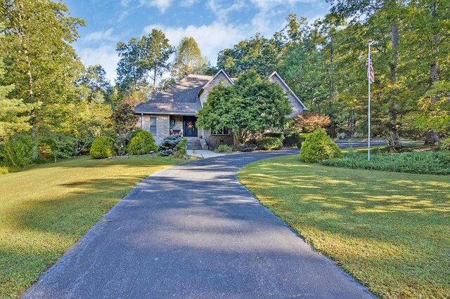 view of front facade featuring driveway, stone siding, and a front yard