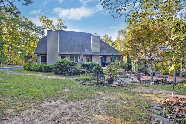 view of front of home featuring a front lawn, a chimney, a patio area, and brick siding