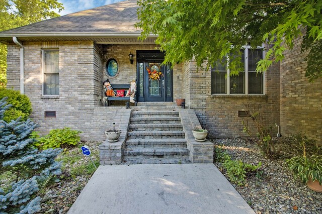 doorway to property featuring crawl space, brick siding, and roof with shingles