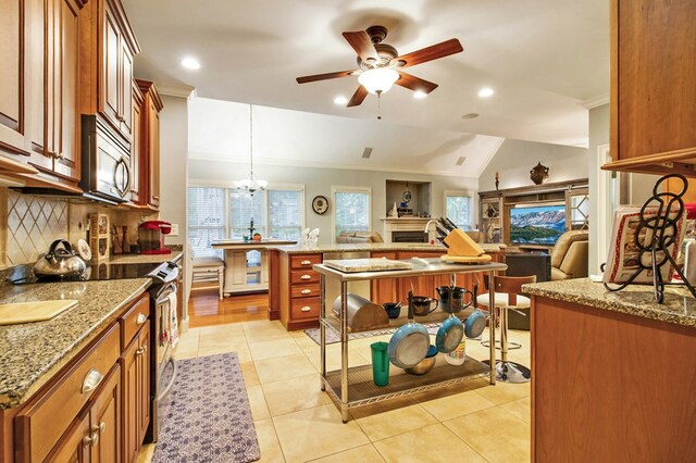 kitchen featuring brown cabinets, decorative light fixtures, lofted ceiling, appliances with stainless steel finishes, and a kitchen island