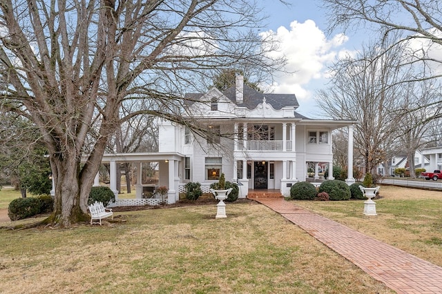 greek revival inspired property with a front yard, a chimney, and a balcony