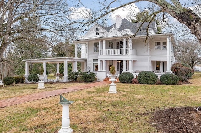 neoclassical home with a front lawn, a chimney, and a balcony