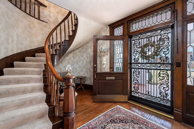 foyer with a wainscoted wall, a healthy amount of sunlight, stairs, dark wood-style floors, and wallpapered walls